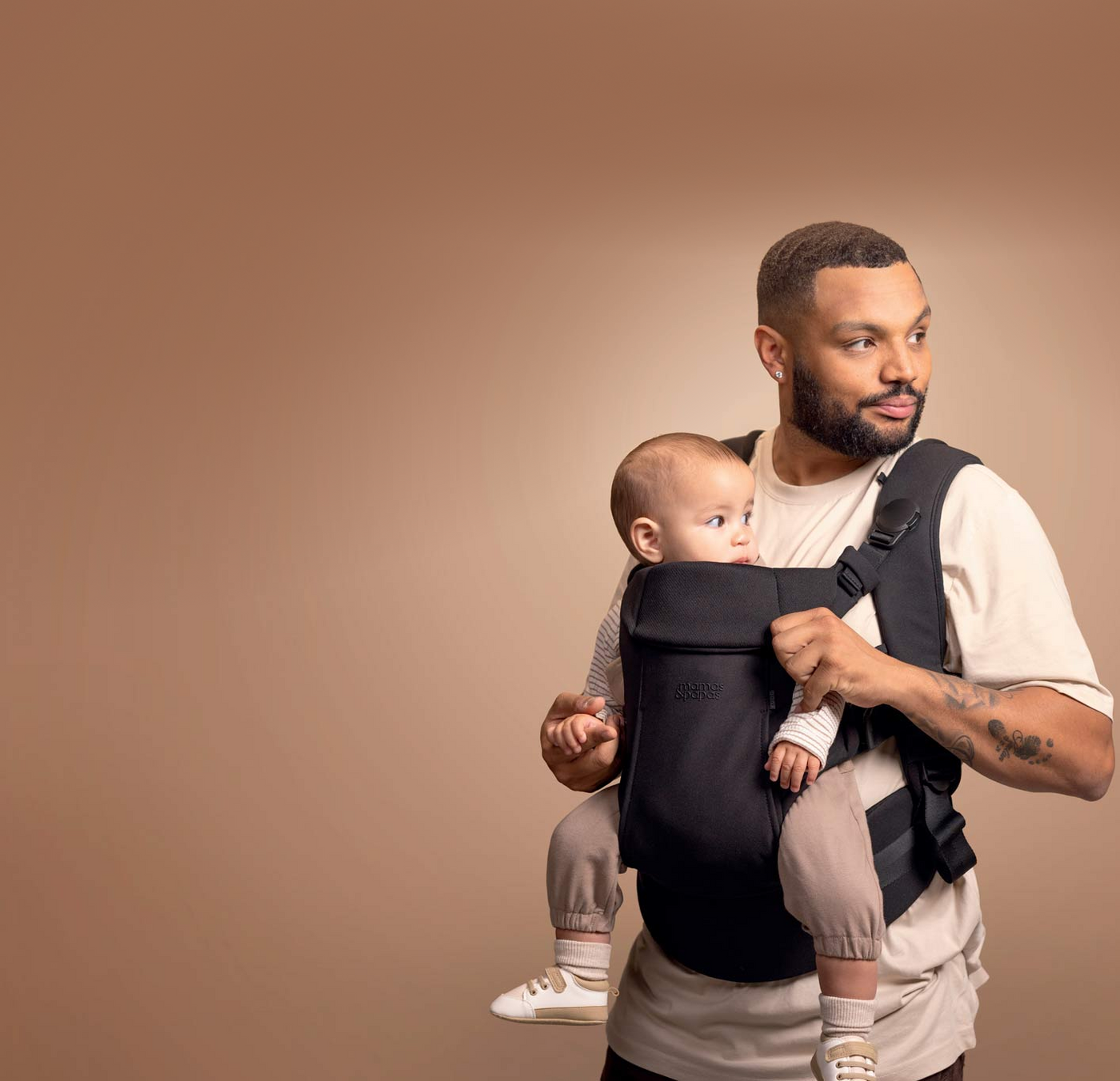 Man holding a baby in a carrier against a brown background
